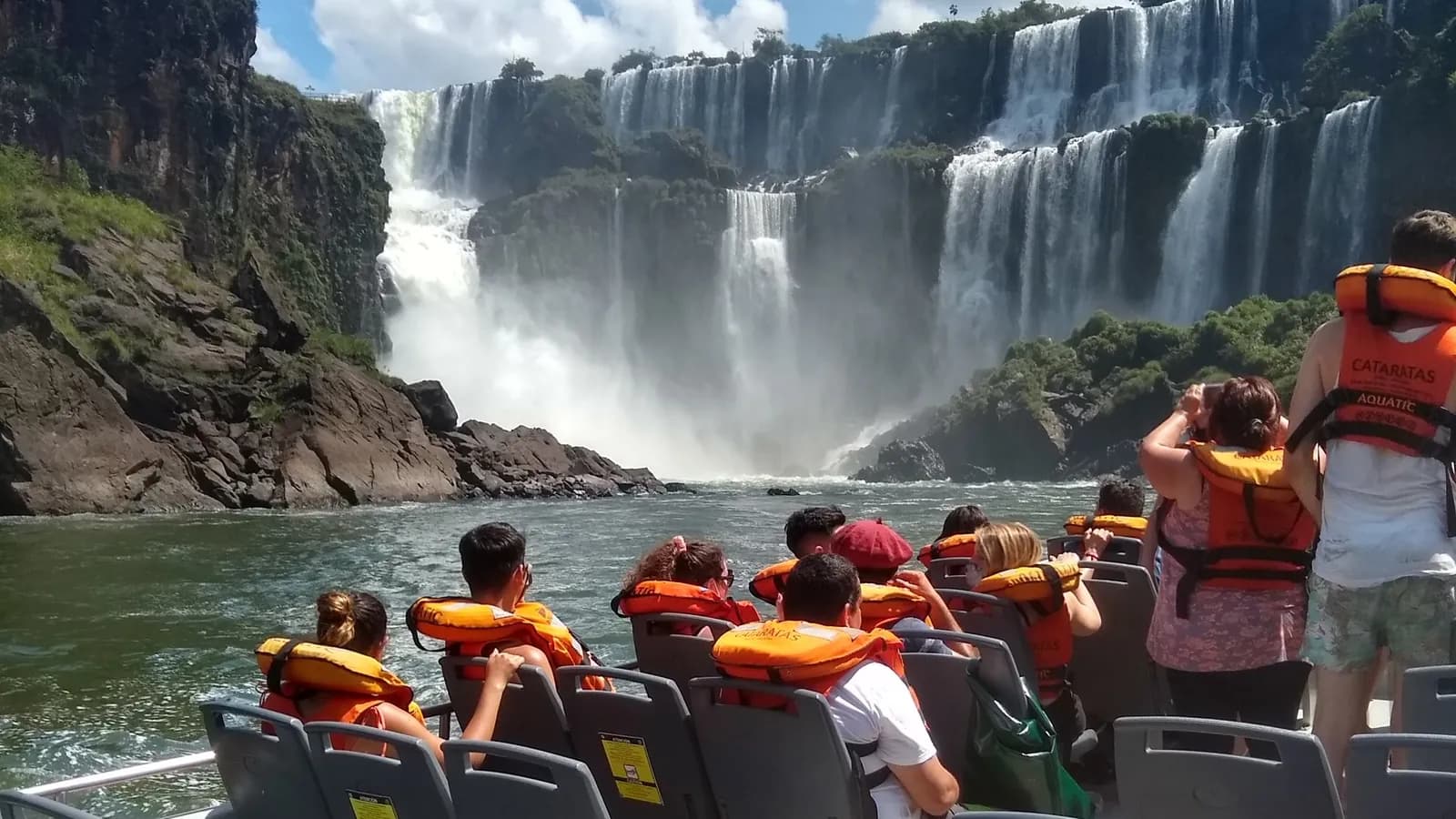 Boat passengers wearing life jackets look up at the waterfalls from the river, Iguazú National Park